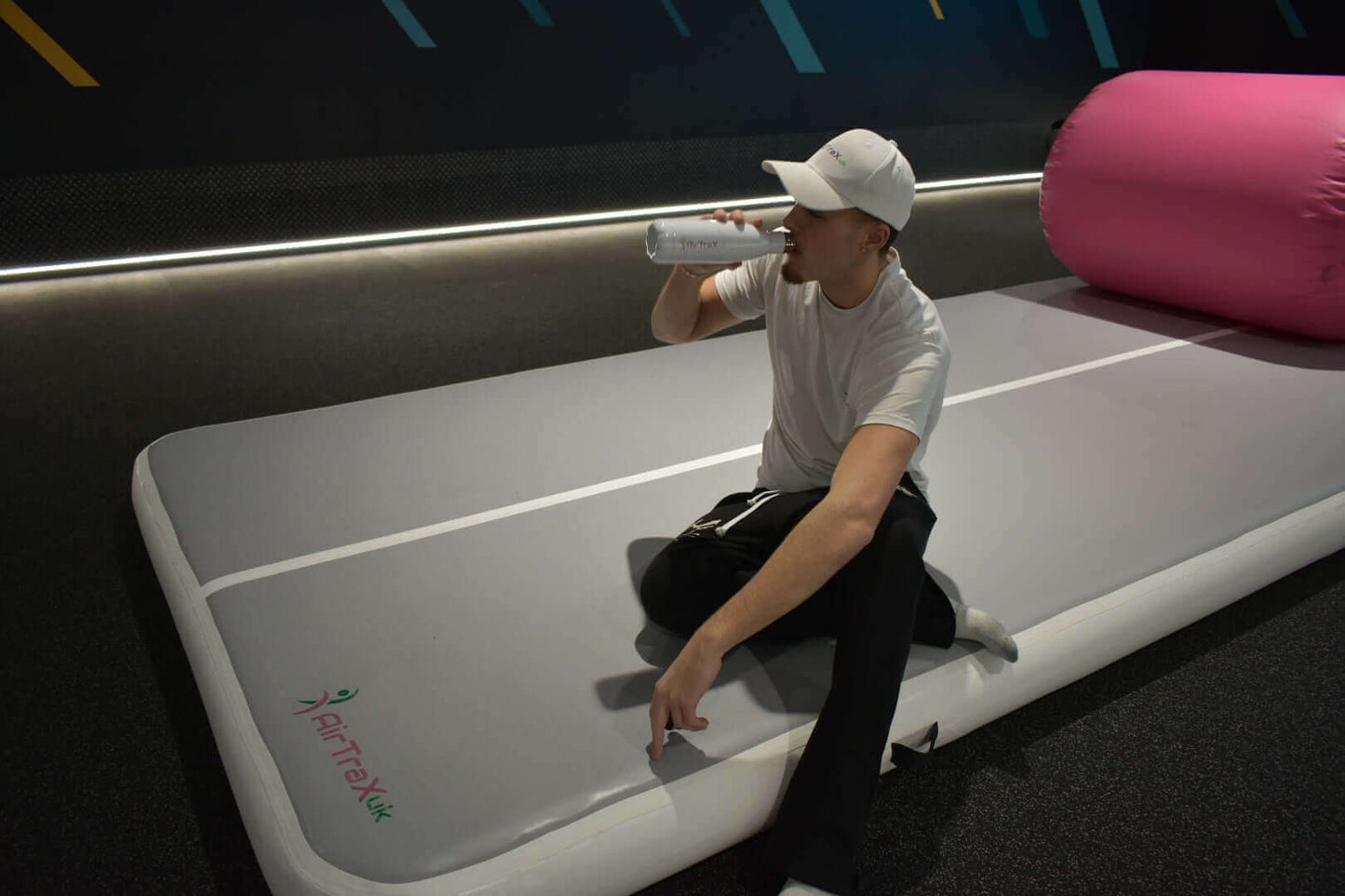 Person sitting on AirTraX Pro air track mat, drinking water in a fitness setting.