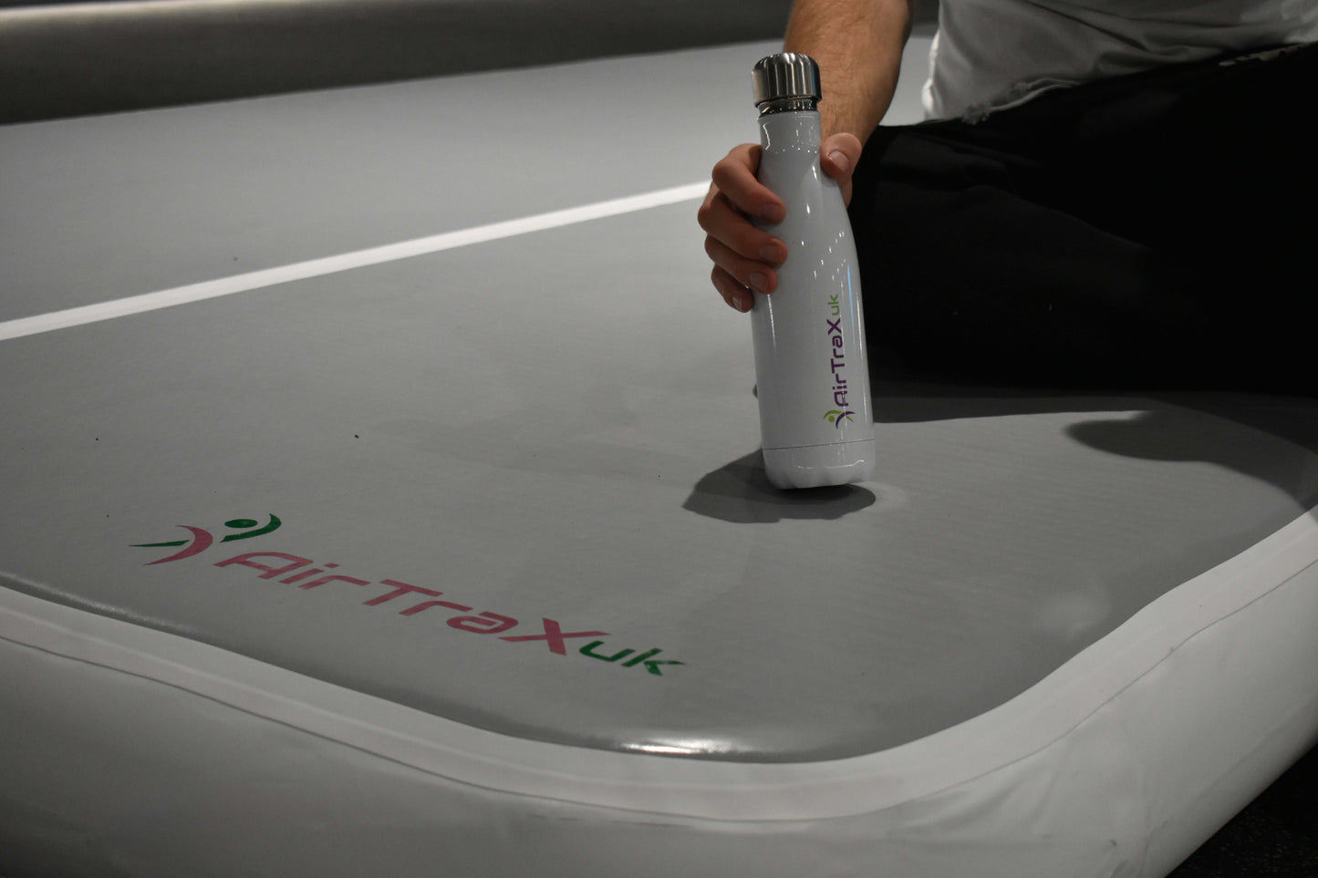 Person holding a water bottle on the AirTraX Pro air track mat with the AirTraX logo visible.
